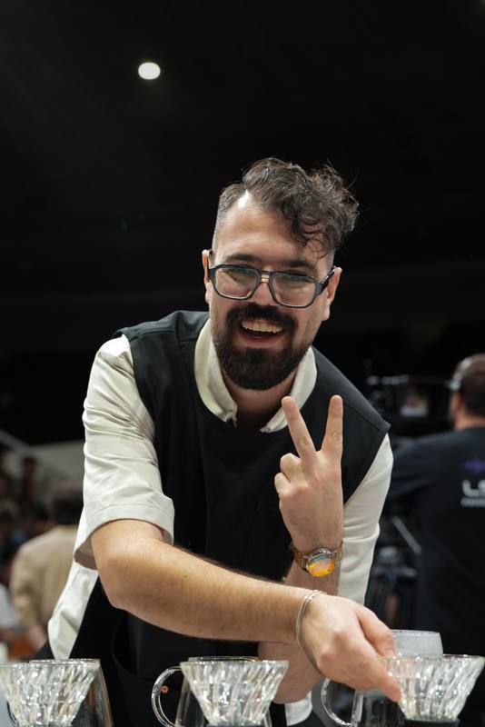 Photograph by Jeff Hann: A laughing competitor in glasses giving a peace sign over his glass drippers