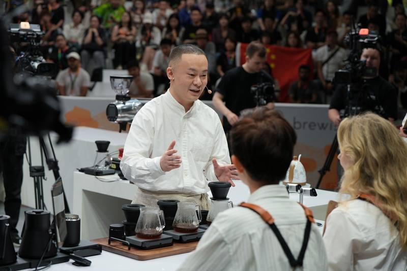 Photograph by Jeff Hann: A competitor in a white shirt talking to the judges, cameras and a packed crowd behind